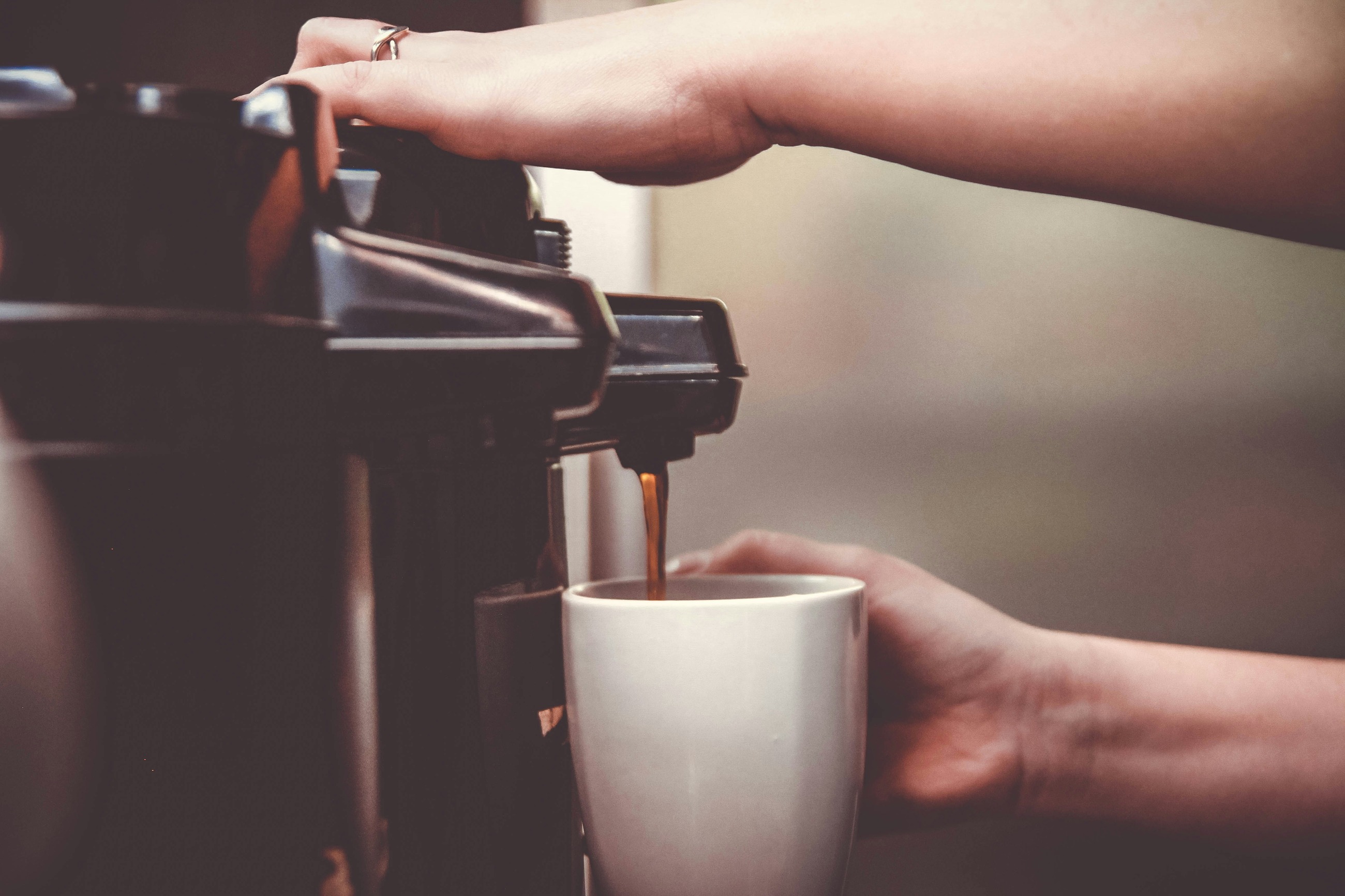 A person pouring freshly brewed coffee into a white cup